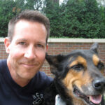 Man smiling with a happy dog outdoors.