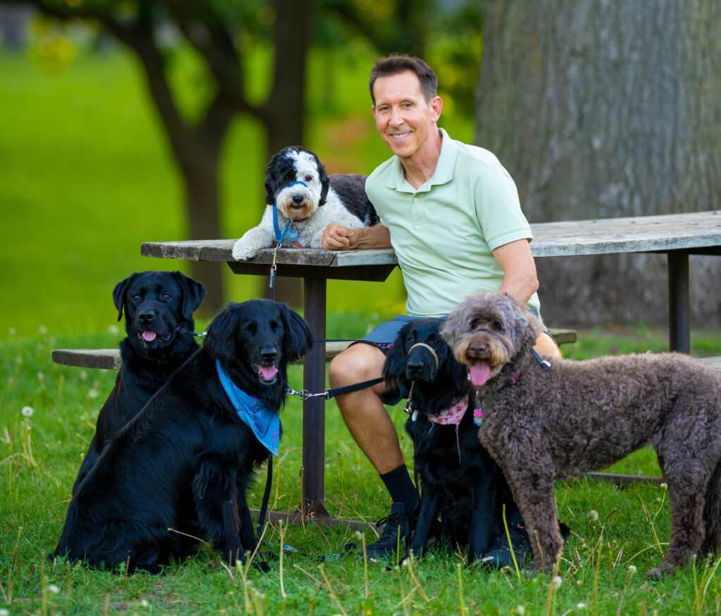 Man sitting outdoors with four dogs of different breeds.