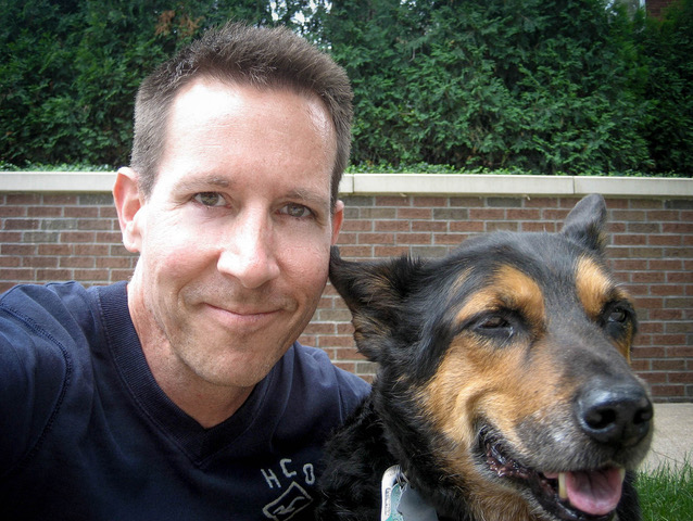 A man smiling next to a happy dog outdoors.